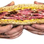 An image of hands holding a sandwich made with RC pastrami